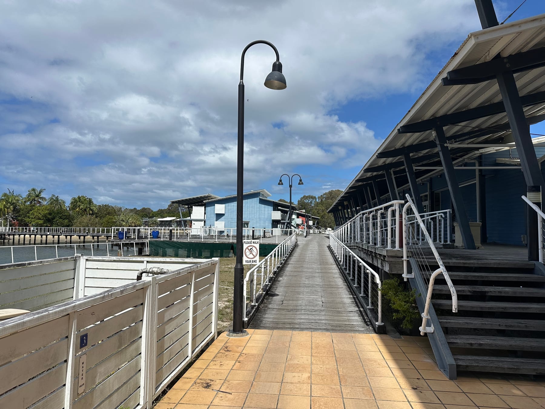 Timber walkway passing blue marina-side buildings toward the former café area