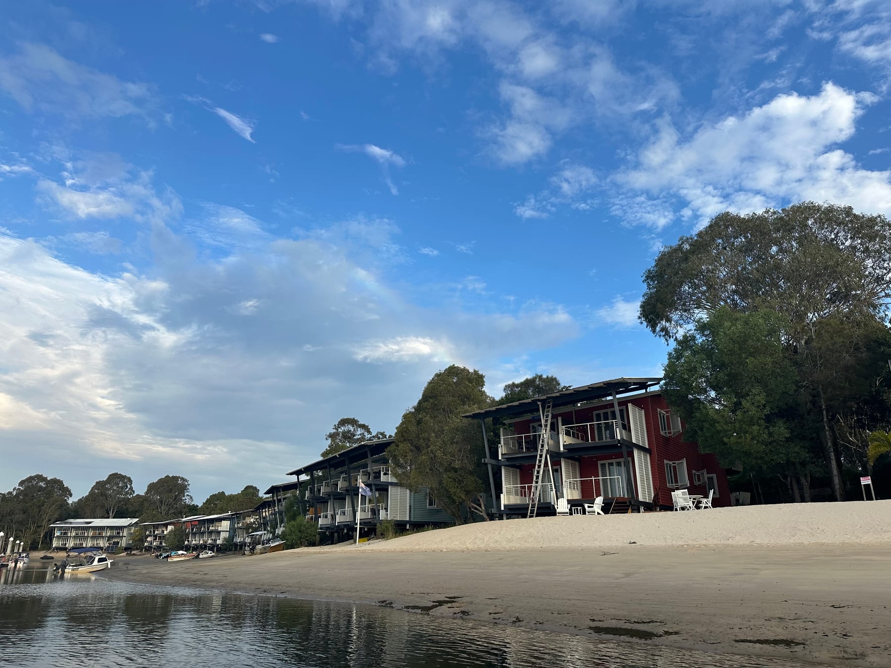 Marina-side buildings on a sandy shoreline beneath a broad blue sky