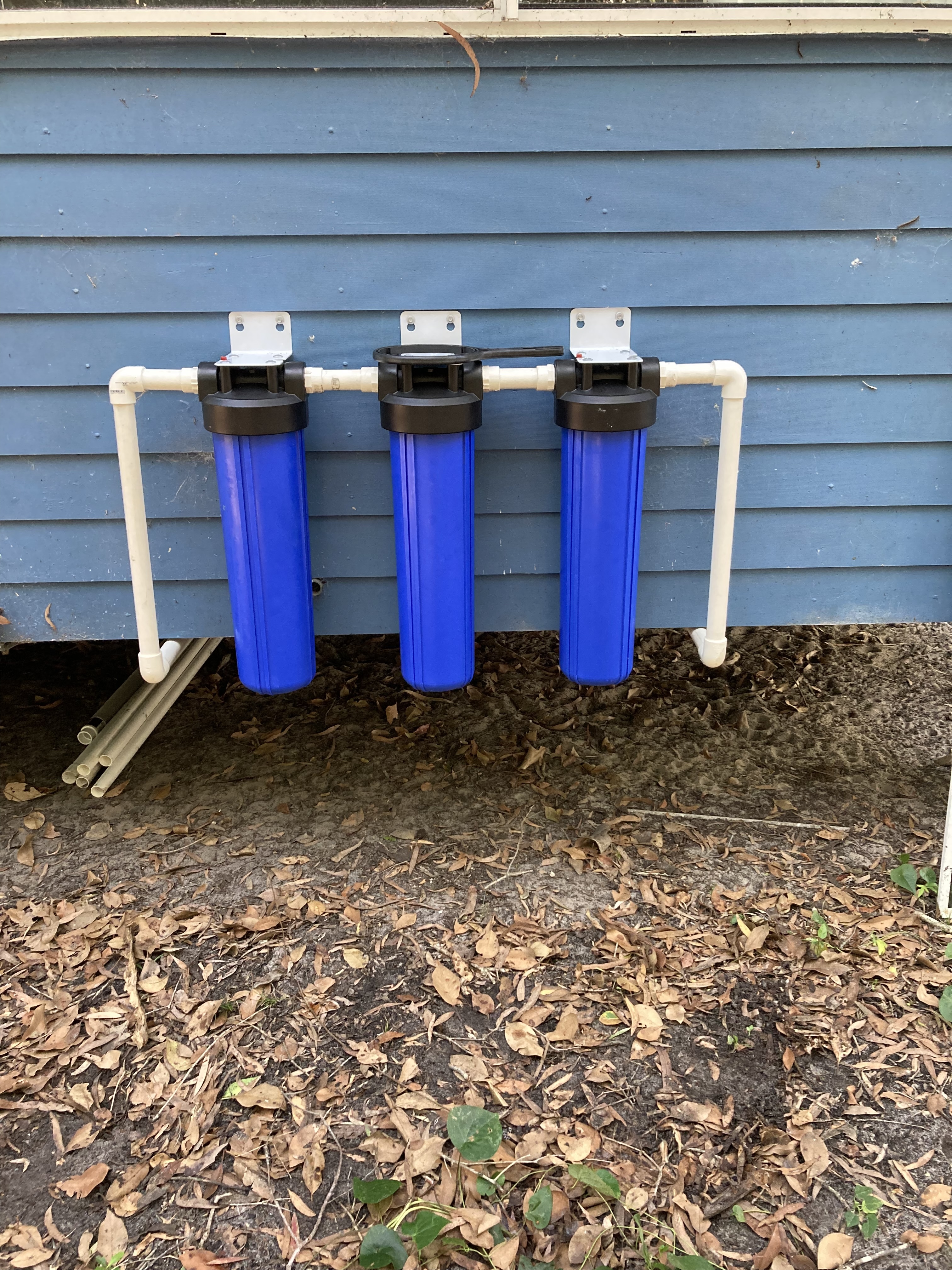 Three water filter housings installed beside a blue villa wall